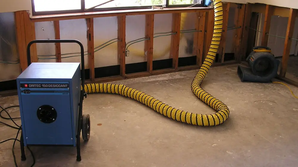 Dehumidifier with yellow ducting beside a wall opened to the studs