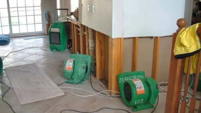 Green air movers on a tile floor next to a wall opened to the studs